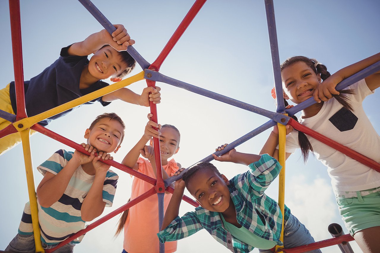Portrait-of-happy-schoolkids-looking-through-dome-climber